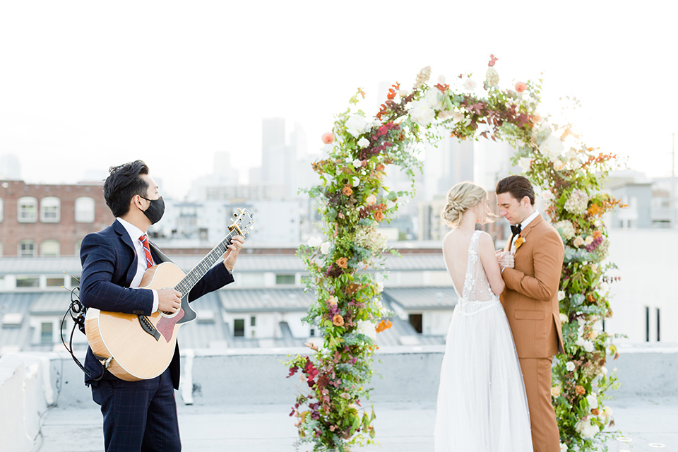  the bride in a white gown with an illusion neckline and hair in a low bun, the groom in a caramel brown suit with a chocolate brown bow tie 