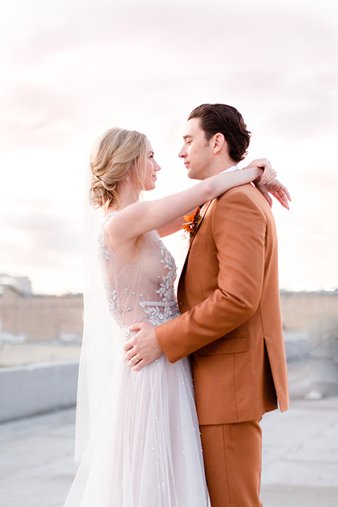  the bride in a white gown with an illusion neckline and hair in a low bun, the groom in a caramel brown suit with a chocolate brown bow tie