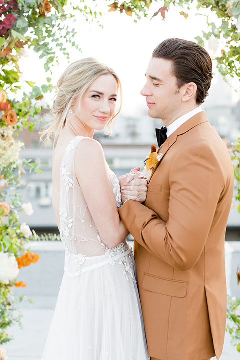  the bride in a white gown with an illusion neckline and hair in a low bun, the groom in a caramel brown suit with a chocolate brown bow tie