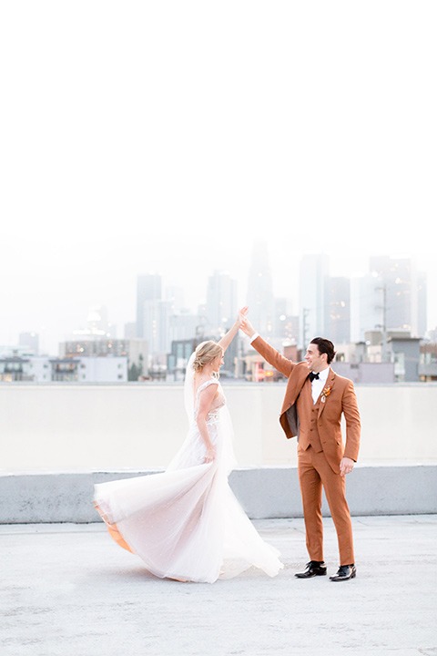  the bride in a white gown with an illusion neckline and hair in a low bun, the groom in a caramel brown suit with a chocolate brown bow tie