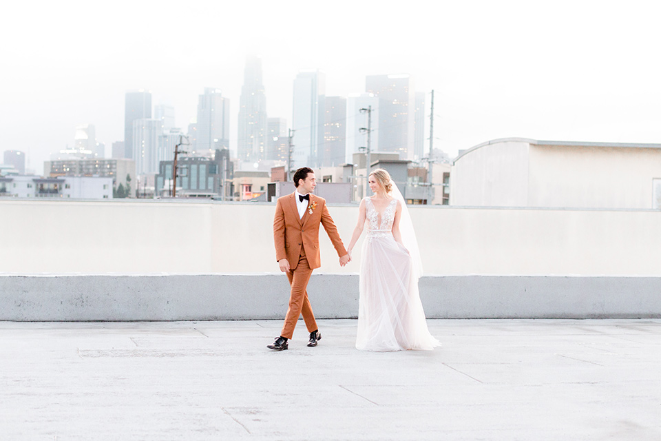  the bride in a white gown with an illusion neckline and hair in a low bun, the groom in a caramel brown suit with a chocolate brown bow tie 