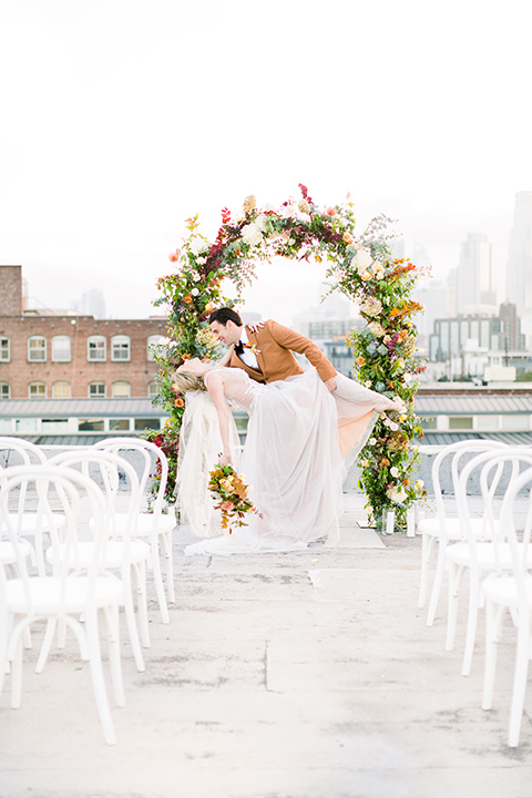  the bride in a white gown with an illusion neckline and hair in a low bun, the groom in a caramel brown suit with a chocolate brown bow tie 