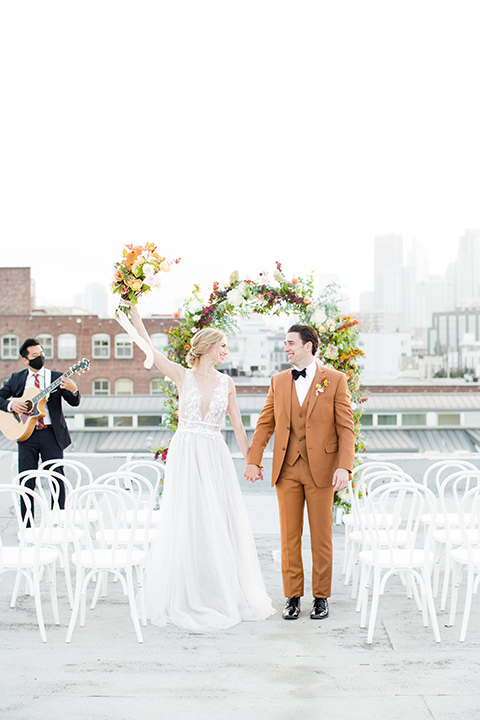  the bride in a white gown with an illusion neckline and hair in a low bun, the groom in a caramel brown suit with a chocolate brown bow tie