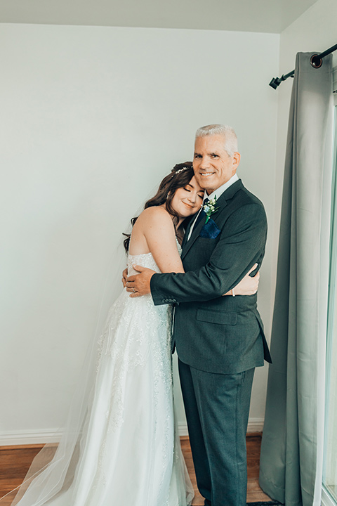  bride in a white gown and the groom in a tan notch lapel suit with a floral tie, the groomsmen in blue suits and the bridesmaids in light blue gowns 