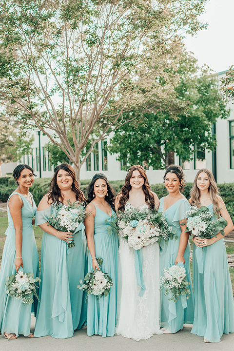  bride in a white gown and the groom in a tan notch lapel suit with a floral tie, the groomsmen in blue suits and the bridesmaids in light blue gowns 