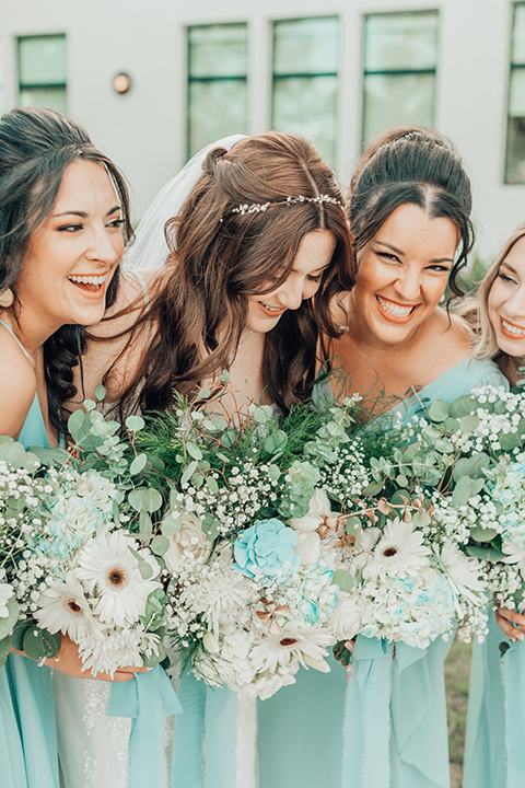  bride in a white gown and the groom in a tan notch lapel suit with a floral tie, the groomsmen in blue suits and the bridesmaids in light blue gowns 