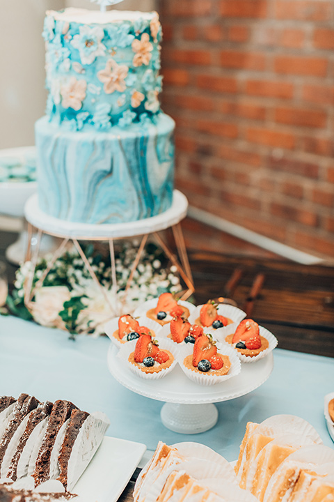  bride in a white gown and the groom in a tan notch lapel suit with a floral tie, the groomsmen in blue suits and the bridesmaids in light blue gowns 