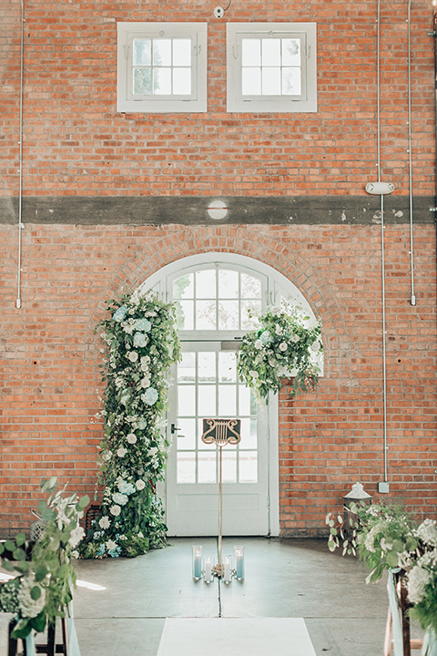  bride in a white gown and the groom in a tan notch lapel suit with a floral tie, the groomsmen in blue suits and the bridesmaids in light blue gowns 