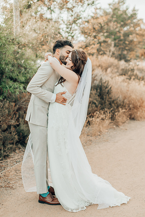  bride in a white gown and the groom in a tan notch lapel suit with a floral tie, the groomsmen in blue suits and the bridesmaids in light blue gowns 