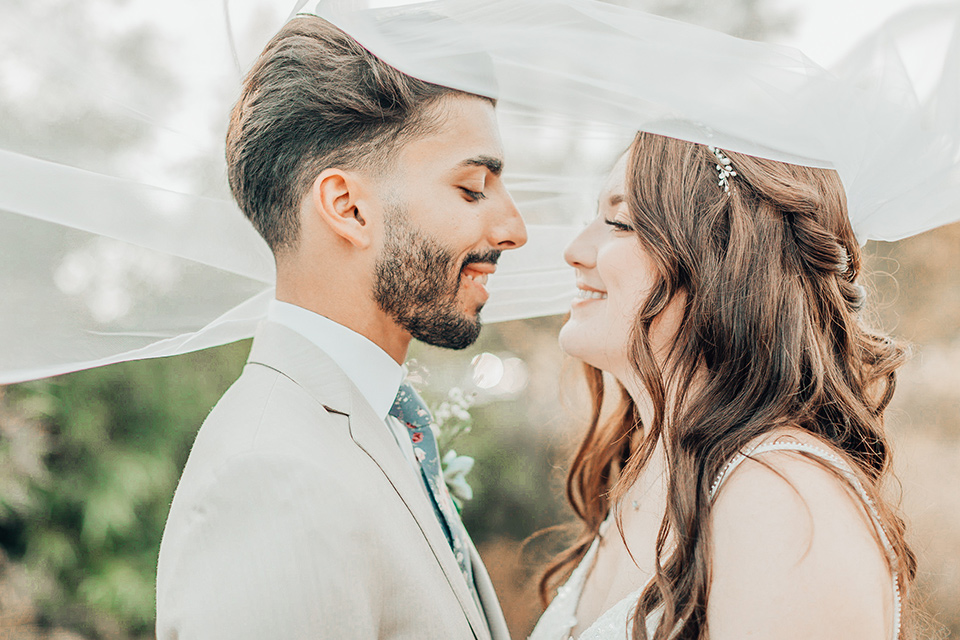  bride in a white gown and the groom in a tan notch lapel suit with a floral tie, the groomsmen in blue suits and the bridesmaids in light blue gowns 