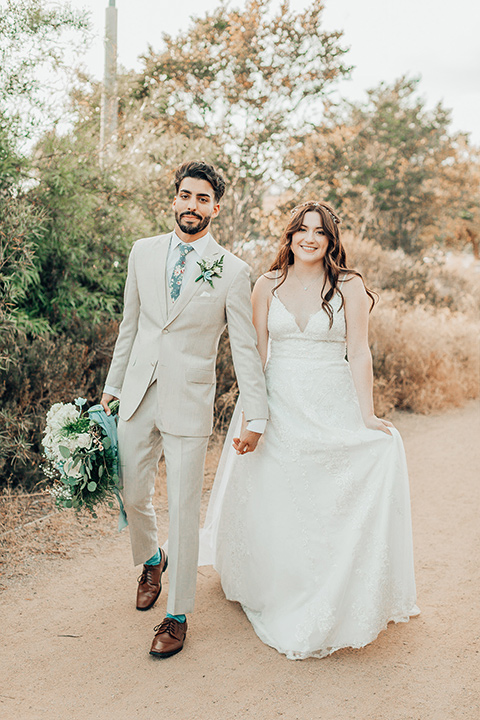  bride in a white gown and the groom in a tan notch lapel suit with a floral tie, the groomsmen in blue suits and the bridesmaids in light blue gowns 