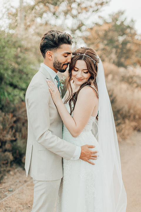  bride in a white gown and the groom in a tan notch lapel suit with a floral tie, the groomsmen in blue suits and the bridesmaids in light blue gowns 