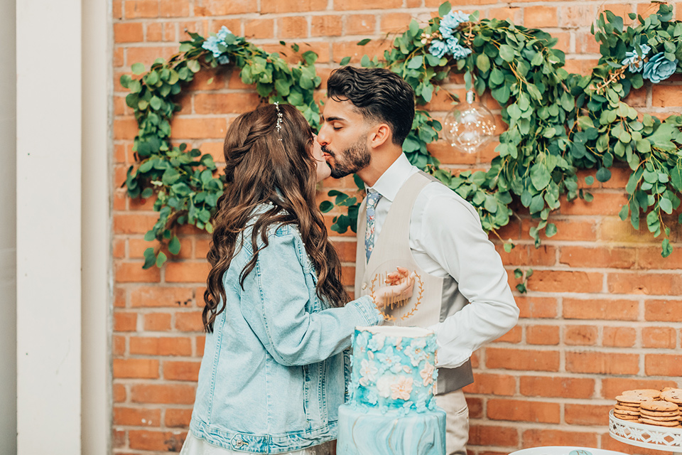  bride in a white gown and the groom in a tan notch lapel suit with a floral tie, the groomsmen in blue suits and the bridesmaids in light blue gowns 