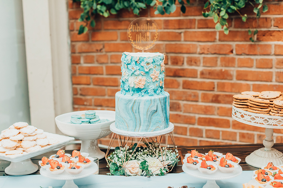  bride in a white gown and the groom in a tan notch lapel suit with a floral tie, the groomsmen in blue suits and the bridesmaids in light blue gowns 