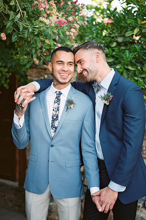  a groom in a blue notch lapel coat and charcoal grey pants and the other groom in a light blue coat and tan pants 