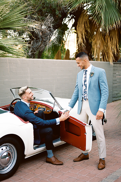  a groom in a blue notch lapel coat and charcoal grey pants and the other groom in a light blue coat and tan pants