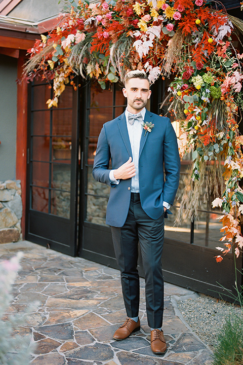  a groom in a blue notch lapel coat and charcoal grey pants and the other groom in a light blue coat and tan pants