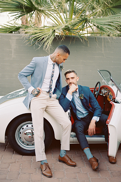  a groom in a blue notch lapel coat and charcoal grey pants and the other groom in a light blue coat and tan pants 