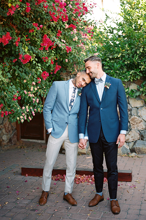  a groom in a blue notch lapel coat and charcoal grey pants and the other groom in a light blue coat and tan pants 