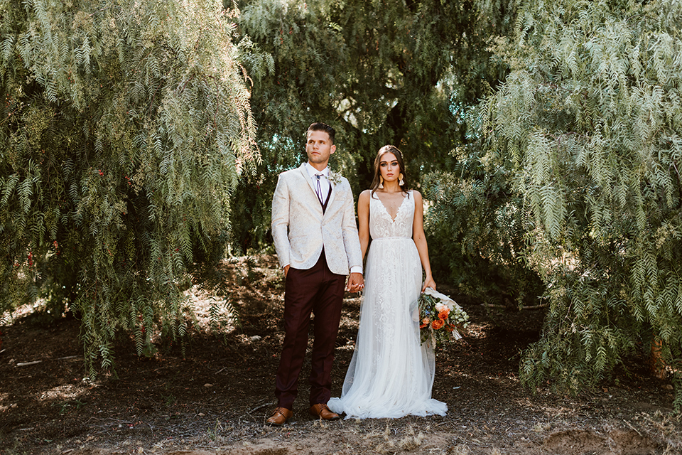  bride in a bohemian gown with chunky earrings and the groom in a ivory paisley tuxedo with burgundy pants and vest 