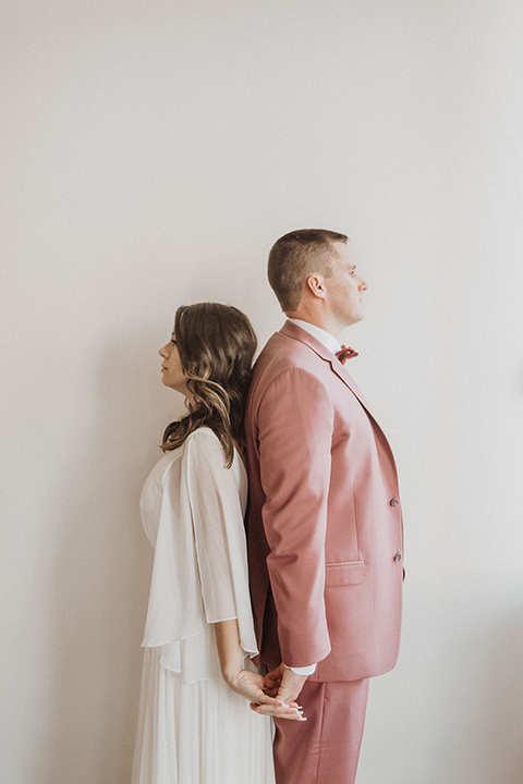  bride in a flowing white gown with flutter sleeves and the groom in a rose-pink suit with a burgundy velvet bow tie 