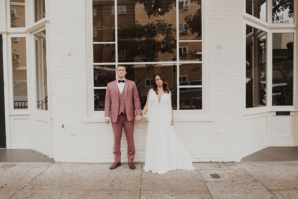  bride in a flowing white gown with flutter sleeves and the groom in a rose-pink suit with a burgundy velvet bow tie 