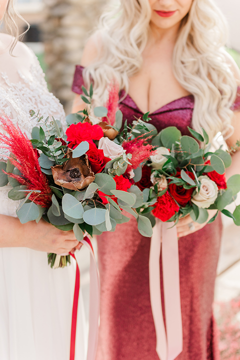  bride in a white and ivory gown with a natural waist and lace long sleeves and the bridesmaid in a red velvet long gown and a floral headpiece