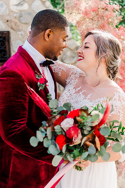  bride in a white and ivory gown with a natural waist and lace long sleeves, the groom in a burgundy velvet tuxedo with a black bow tie 