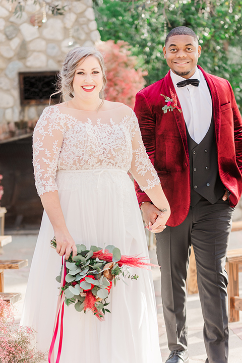  bride in a white and ivory gown with a natural waist and lace long sleeves, the groom in a burgundy velvet tuxedo with a black bow tie 