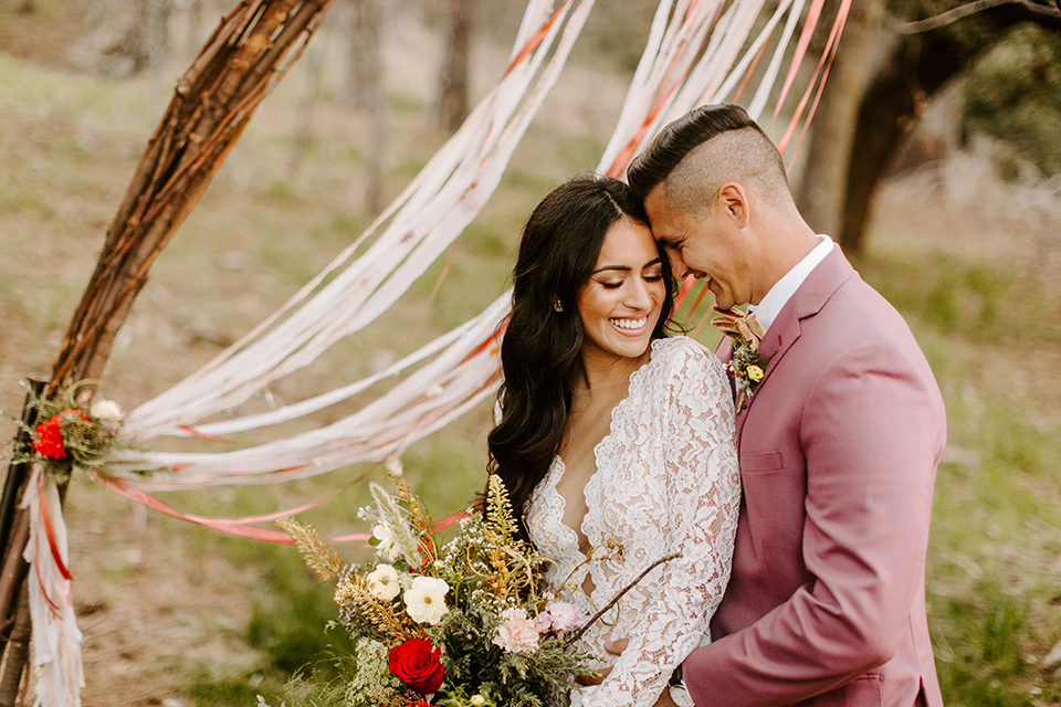  bride in a lace gown with long sleeves and the groom in a rose pink suit with a gold velvet bow tie 