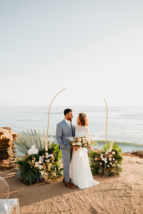  bride in a lace gown with ¾ sleeves and a gold hairpiece and the groom in a light blue suit with no tie 