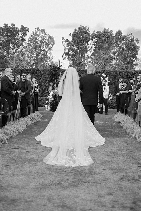  a chic black and white wedding with modern touches with the groom in a white tuxedo and the bride in a white ballgown and the bridesmaids and groomsmen in black dresses/tuxedos – bride walking down the aisle 