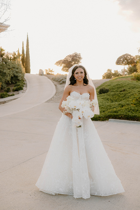  a chic black and white wedding with modern touches with the groom in a white tuxedo and the bride in a white ballgown and the bridesmaids and groomsmen in black dresses/tuxedos – bride walking in her dress toward the camera 