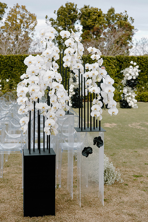  a chic black and white wedding with modern touches with the groom in a white tuxedo and the bride in a white ballgown and the bridesmaids and groomsmen in black dresses/tuxedos – modern ceremony space and décor