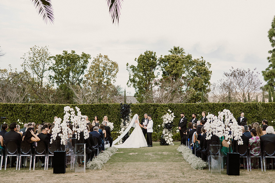  a chic black and white wedding with modern touches with the groom in a white tuxedo and the bride in a white ballgown and the bridesmaids and groomsmen in black dresses/tuxedos – ceremony 