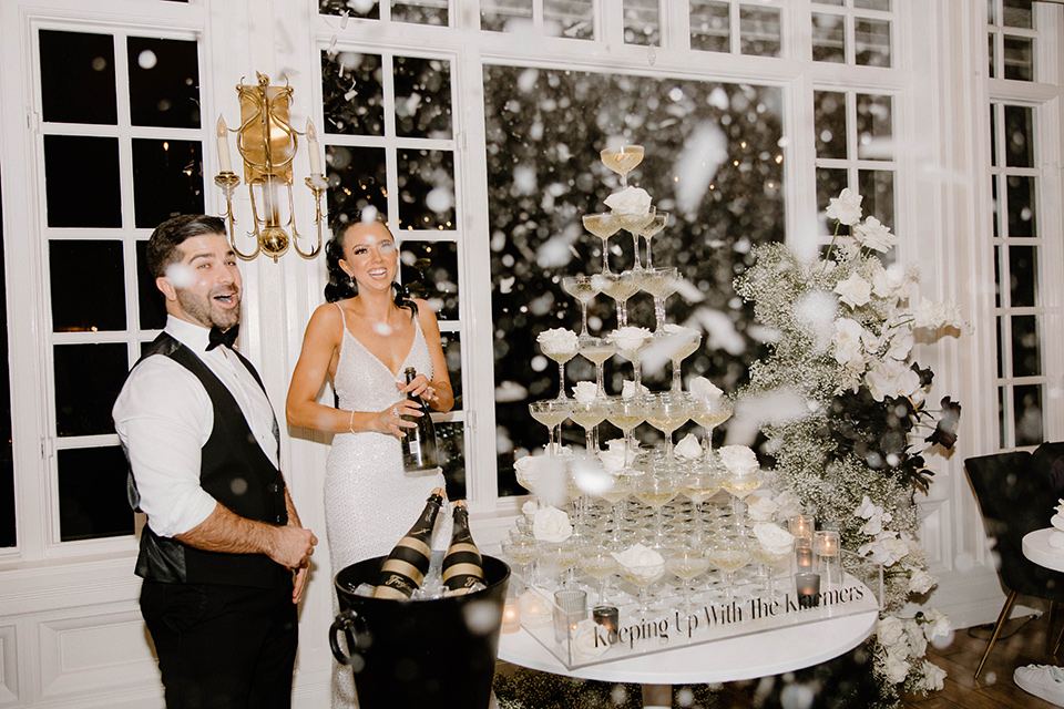  a chic black and white wedding with modern touches with the groom in a white tuxedo and the bride in a white ballgown and the bridesmaids and groomsmen in black dresses/tuxedos – couple pouring champagne 
