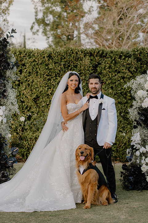  a chic black and white wedding with modern touches with the groom in a white tuxedo and the bride in a white ballgown and the bridesmaids and groomsmen in black dresses/tuxedos – couple with their dog 