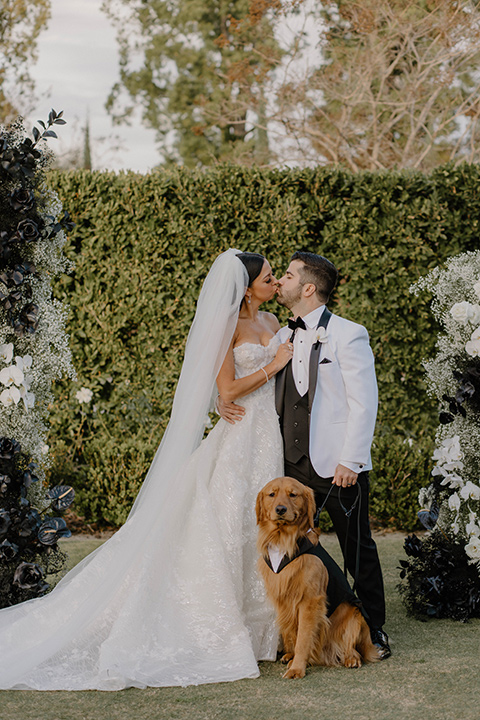  a chic black and white wedding with modern touches with the groom in a white tuxedo and the bride in a white ballgown and the bridesmaids and groomsmen in black dresses/tuxedos – couple with their dog 