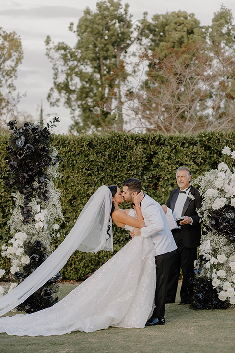  a chic black and white wedding with modern touches with the groom in a white tuxedo and the bride in a white ballgown and the bridesmaids and groomsmen in black dresses/tuxedos – first kiss 