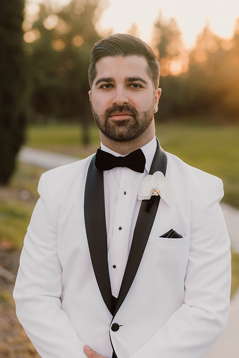  a chic black and white wedding with modern touches with the groom in a white tuxedo and the bride in a white ballgown and the bridesmaids and groomsmen in black dresses/tuxedos – groom smiling 