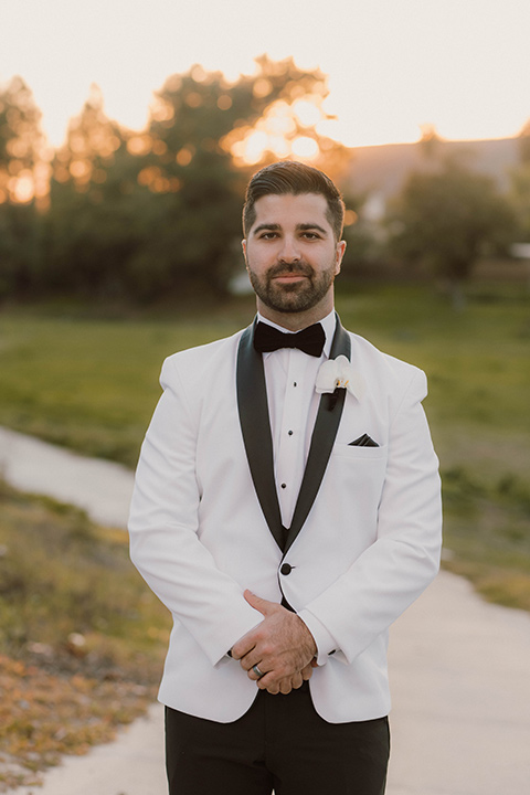  a chic black and white wedding with modern touches with the groom in a white tuxedo and the bride in a white ballgown and the bridesmaids and groomsmen in black dresses/tuxedos – groom in his tuxedo 