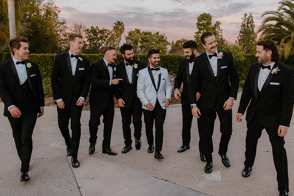  a chic black and white wedding with modern touches with the groom in a white tuxedo and the bride in a white ballgown and the bridesmaids and groomsmen in black dresses/tuxedos – groomsmen in a line 