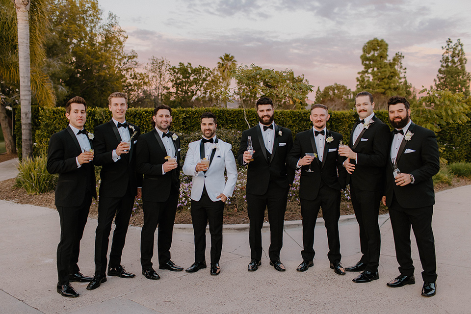  a chic black and white wedding with modern touches with the groom in a white tuxedo and the bride in a white ballgown and the bridesmaids and groomsmen in black dresses/tuxedos – groomsmen in a line 