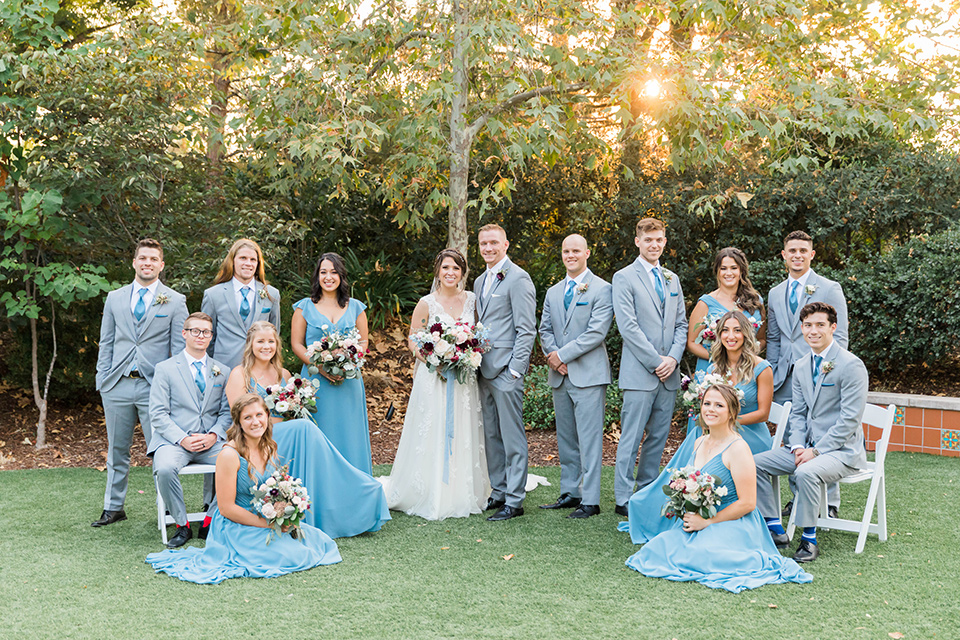  baseball inspired wedding with light blue and white details – groom and groomsmen in grey suits and the bridesmaids in dusty blue gowns and the bride in a lace bridal gown 