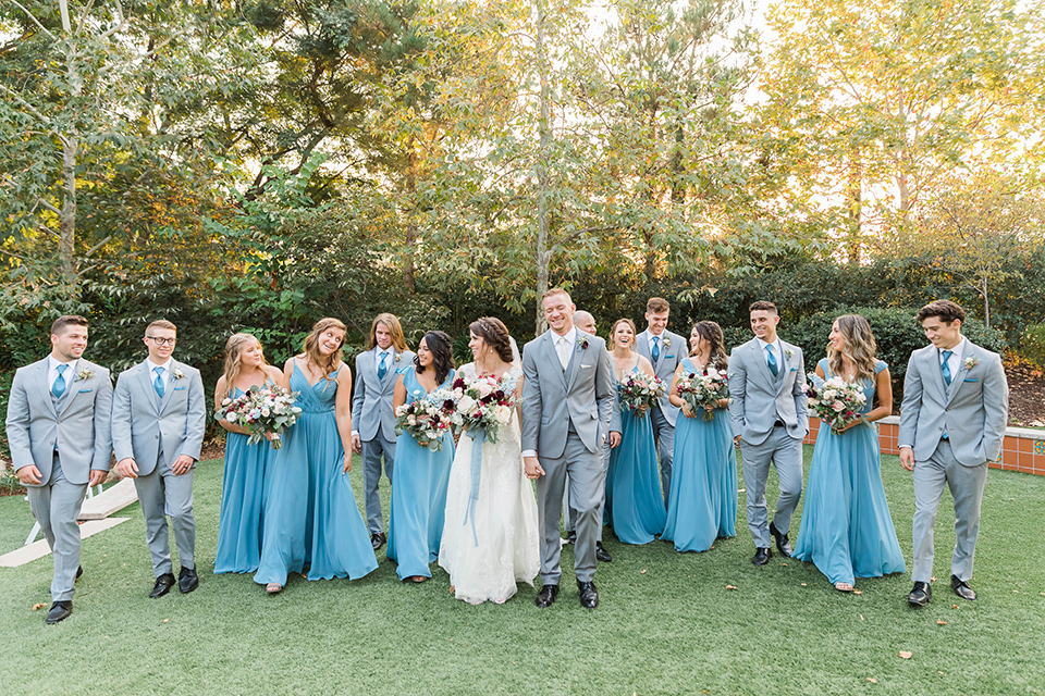  baseball inspired wedding with light blue and white details – groom and groomsmen in grey suits and the bridesmaids in dusty blue gowns and the bride in a lace bridal gown 