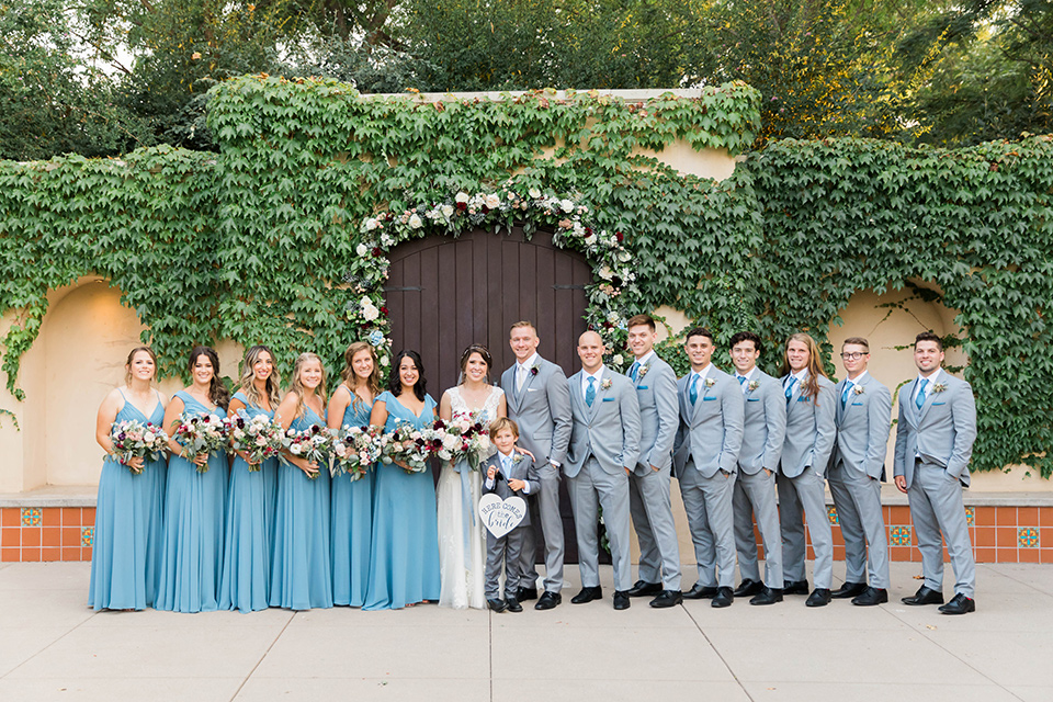  baseball inspired wedding with light blue and white details – groom and groomsmen in grey suits and the bridesmaids in dusty blue gowns and the bride in a lace bridal gown 