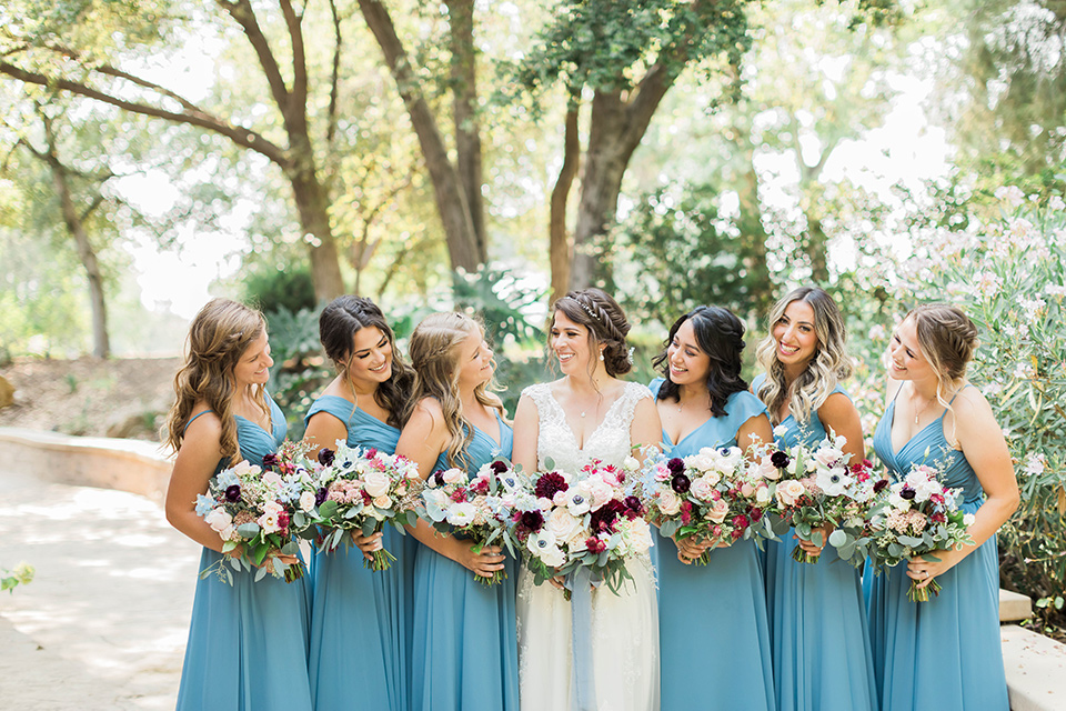  baseball inspired wedding with light blue and white details – groom and groomsmen in grey suits and the bridesmaids in dusty blue gowns and the bride in a lace bridal gown 