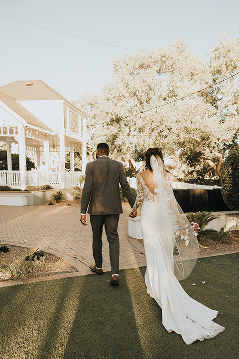  A dreamy amber toned wedding in Arizona at a wedgewood wedding venue – with the bride in a long sleeve lace gown and the bridesmaids in burnt orange dresses and the groom in a café brown suit and the groomsmen in a tan suit – couple walking away from the camera