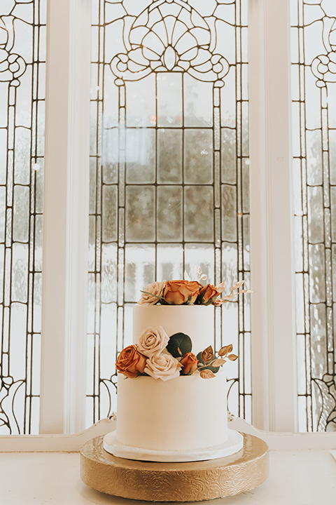  A dreamy amber toned wedding in Arizona at a wedgewood wedding venue – with the bride in a long sleeve lace gown and the bridesmaids in burnt orange dresses and the groom in a café brown suit and the groomsmen in a tan suit – two tiered white cake with flowers