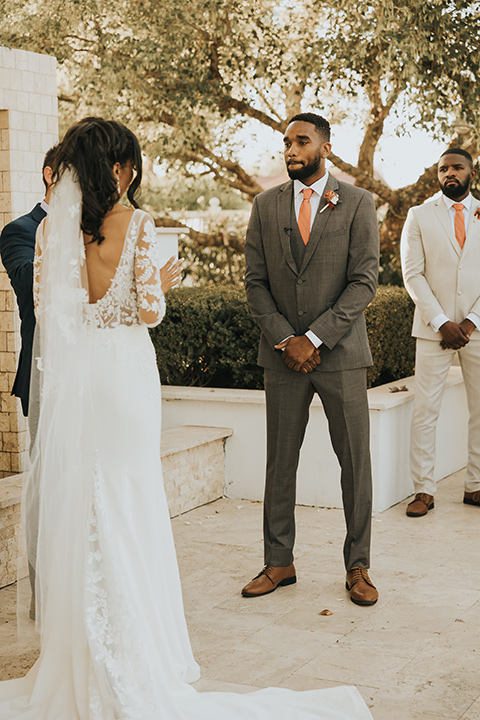  A dreamy amber toned wedding in Arizona at a wedgewood wedding venue – with the bride in a long sleeve lace gown and the bridesmaids in burnt orange dresses and the groom in a café brown suit and the groomsmen in a tan suit – couple at the ceremony